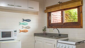 A compact kitchen with a microwave, sink, and stove. There are decorative fish-shaped signs on the wall. - Bon Amour Punta del Diablo (Punta del Diablo)