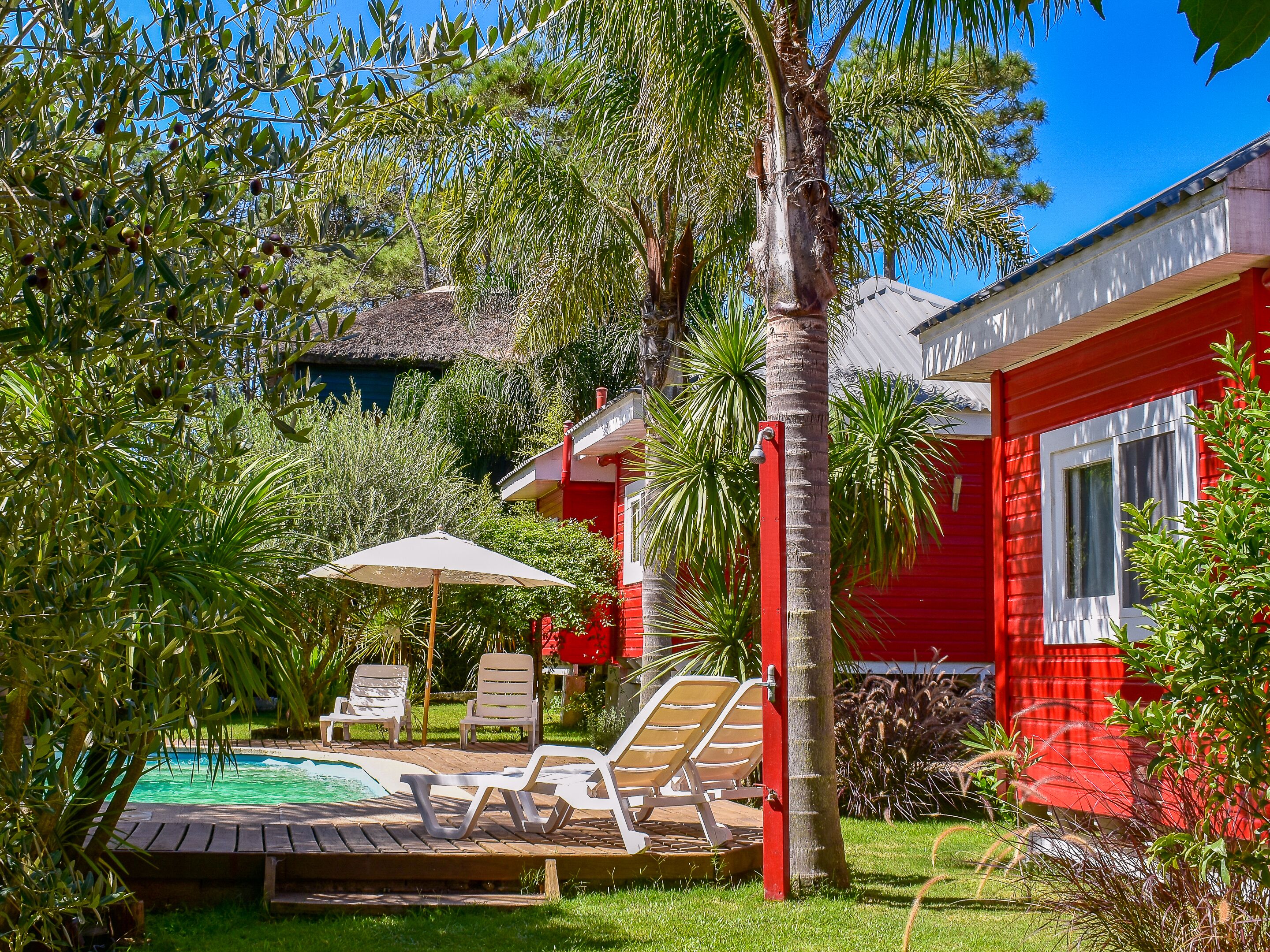 Um edifício vermelho com piscina, rodeado por vegetação exuberante e palmeiras.
