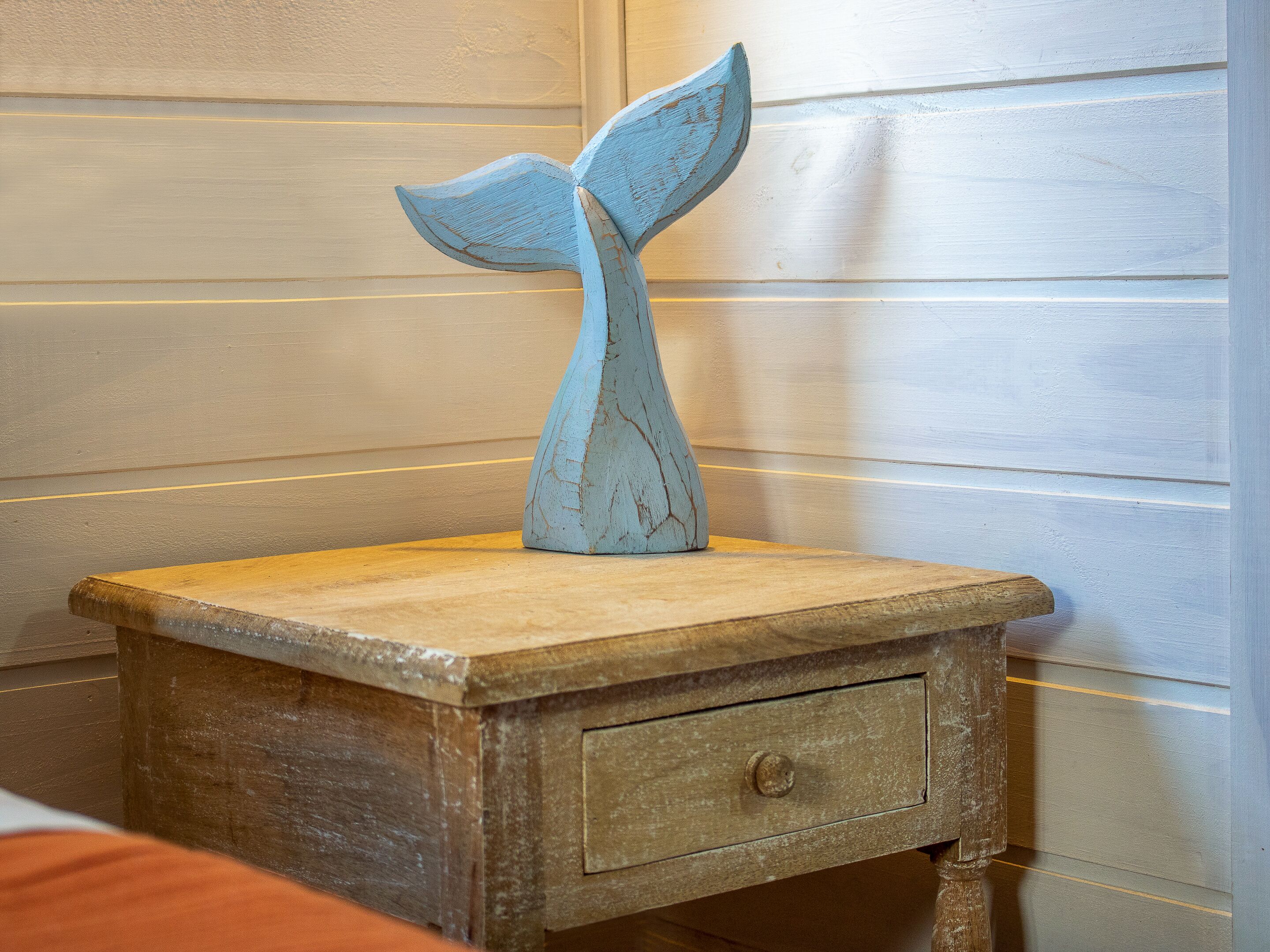 A wooden nightstand with a drawer and a decorative whale tail sculpture.