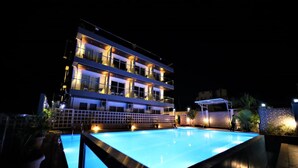 Un hotel de varios pisos con piscina, de noche.