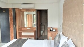 Habitación de hotel con cama, tocador de madera, espejo, baño y kitchenette.