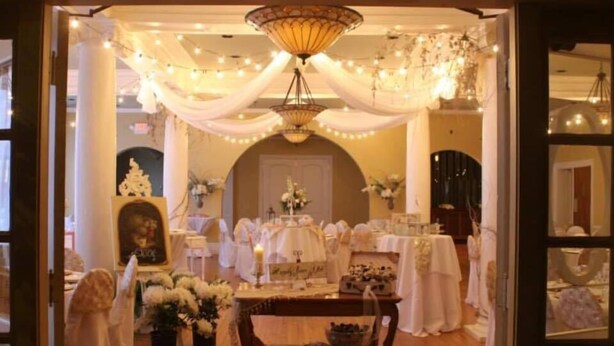 An elegantly decorated room with a chandelier, draped fabric, and floral arrangements. - Stearns Hotel (Ludington)