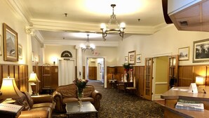 A hotel lobby with a reception desk, leather seating, a chandelier, and a patterned carpet. - Stearns Hotel (Ludington)