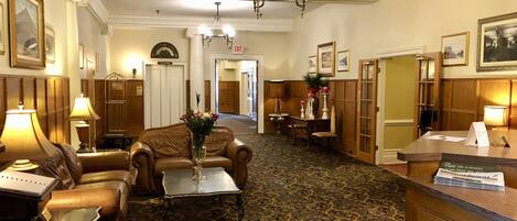 A hotel lobby with a reception desk, leather seating, a chandelier, and a patterned carpet.
