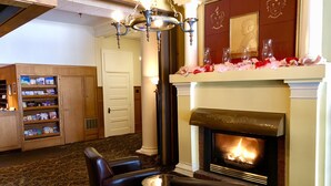 A lobby with a fireplace, leather chairs, a small table, a bookshelf, and a chandelier. - Stearns Hotel (Ludington)