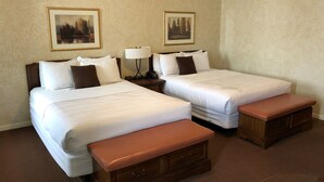 A hotel room with two single beds, a nightstand with a lamp, a telephone, and a small wooden bench. - Stearns Hotel (Ludington)