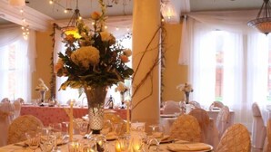 A banquet hall with round tables set for a formal event, featuring floral centerpieces and candlelight. - Stearns Hotel (Ludington)