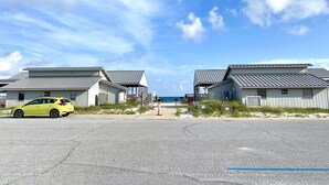 A row of beachside cabins with a view of the ocean, a parking area with a yellow car, and a clear sky. - New! 5 min to beach! Clean, modern and spacious-King mattress on Primary room  (Pensacola)