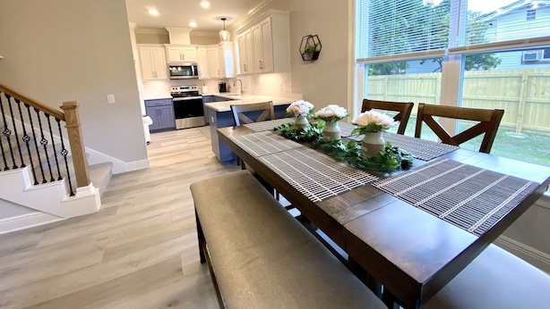 A modern kitchen with white cabinets, a stainless steel oven, and a dining area with a wooden table and chairs. - New! 5 min to beach! Clean, modern and spacious-King mattress on Primary room  (Pensacola)