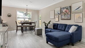 A living room with a blue sectional sofa, a dining table with chairs, and a chandelier. - New! 5 min to beach! Clean, modern and spacious-King mattress on Primary room  (Pensacola)