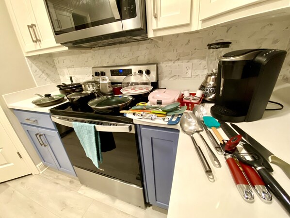 A kitchen with a stove, microwave, and coffee maker. There are utensils and dishes on the counter. - New! 5 min to beach! Clean, modern and spacious-King mattress on Primary room (Pensacola)