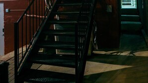 A staircase leading to a door with a security camera above it, a red brick wall, and a metal railing.