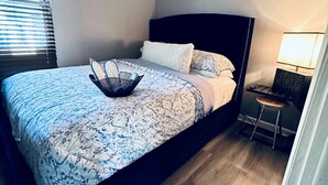 A bedroom with a bed, a bedside table, a lamp, and a window with blinds.