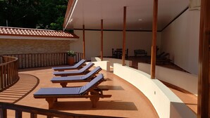Un área de descanso al aire libre con sol, sillones de madera y una zona de estar cubierta.