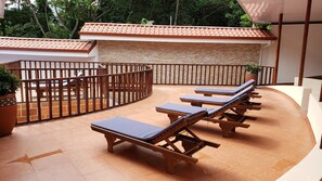 A sunlit outdoor area with a curved seating arrangement, a stone wall, and a tiled roof. - Beautiful 3 Bedroom 3 Bath Condo with Private Courtyard and Attached Garage (La Fortuna)