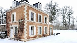 A two-story brick building with white shutters, a snow-covered landscape, and leafless trees. - Gîte Vichy - 4 Chambres, Situé Dans le Parc du Château de Charmeil (Charmeil)