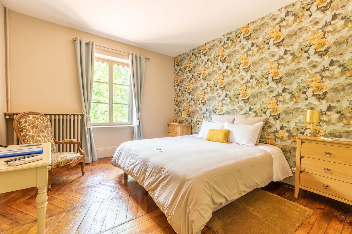 Ein Schlafzimmer mit einem großen Bett, einem Holzstuhl, einem Schreibtisch und einer Heizung.
