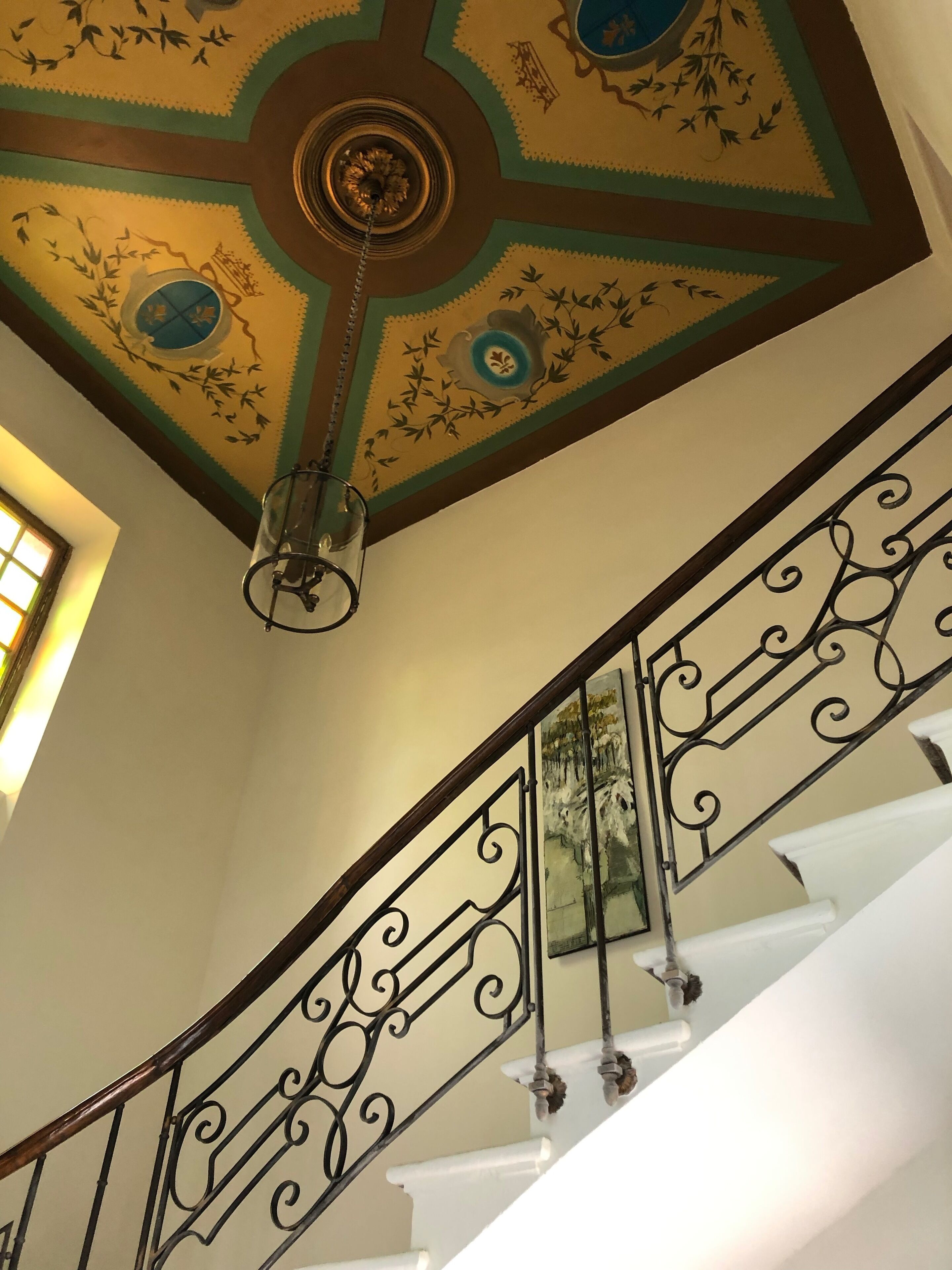 Una escalera con barandillas de metal decorativas y un techo ornamental con motivos florales.