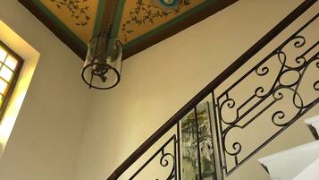 Una escalera con barandillas de metal decorativas y un techo ornamental con motivos florales.