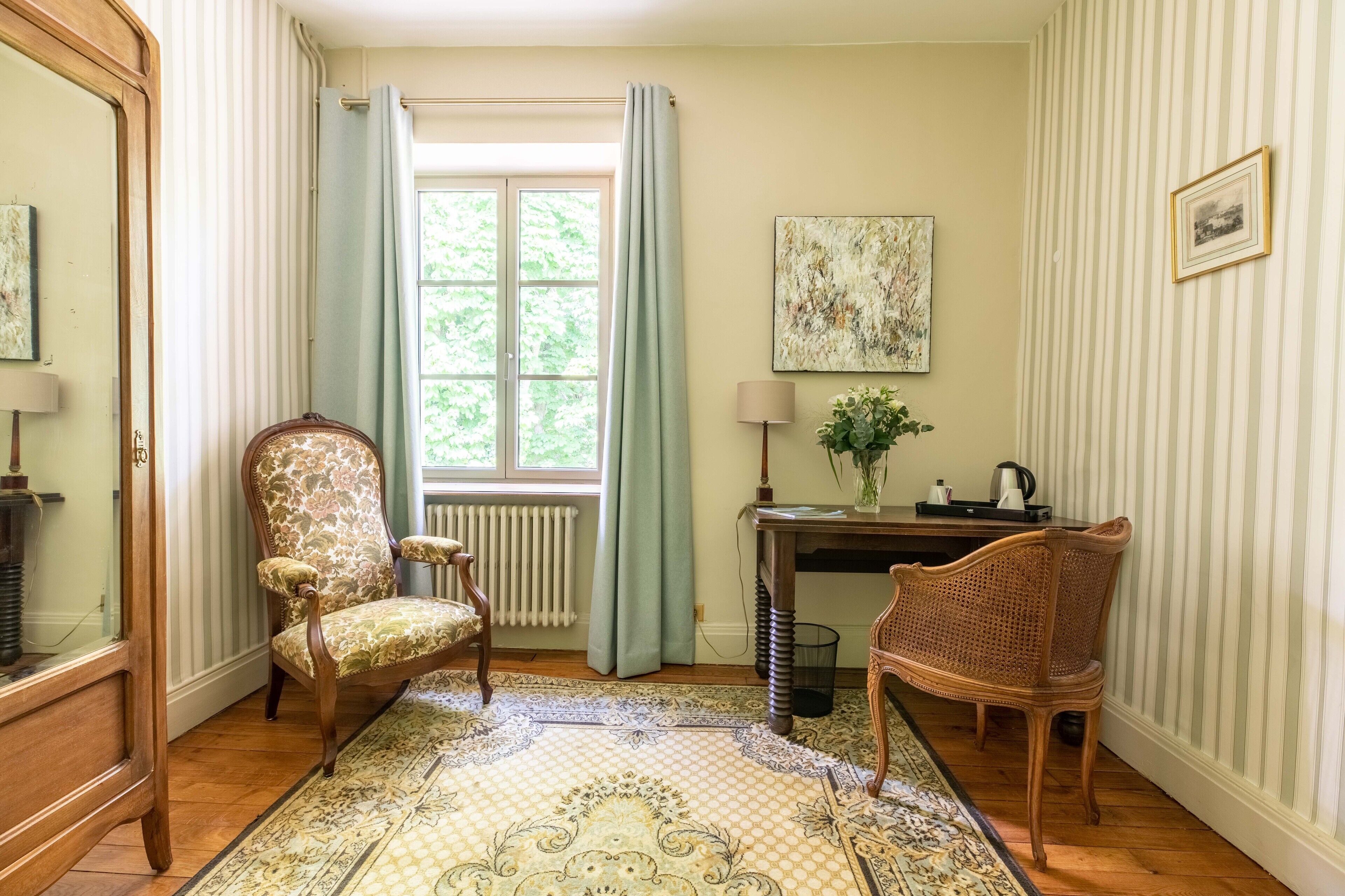 A room with a large window, a radiator, a desk, two chairs, and a patterned rug.