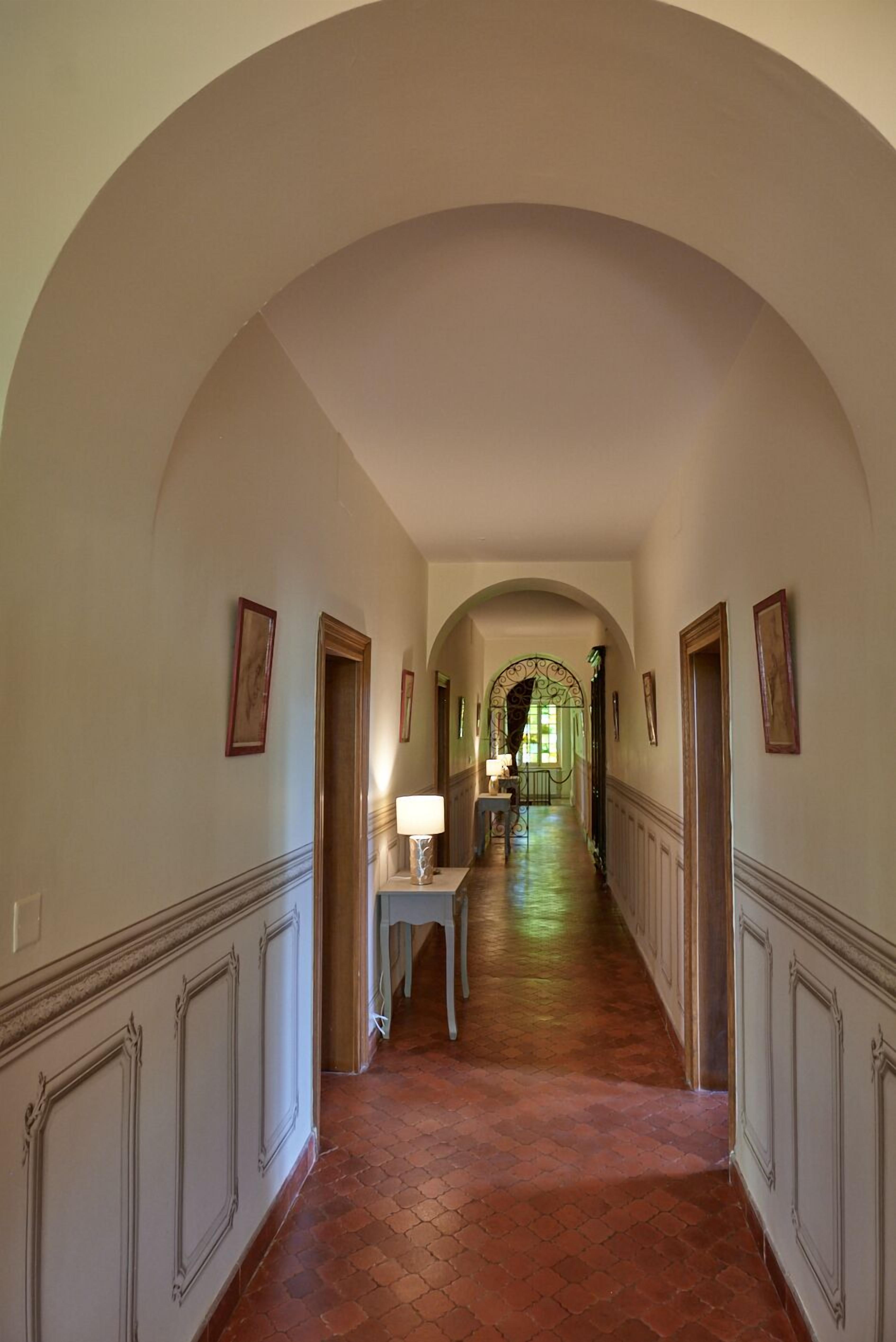 A corridor with arched ceilings, framed pictures on the walls, and a wooden floor.