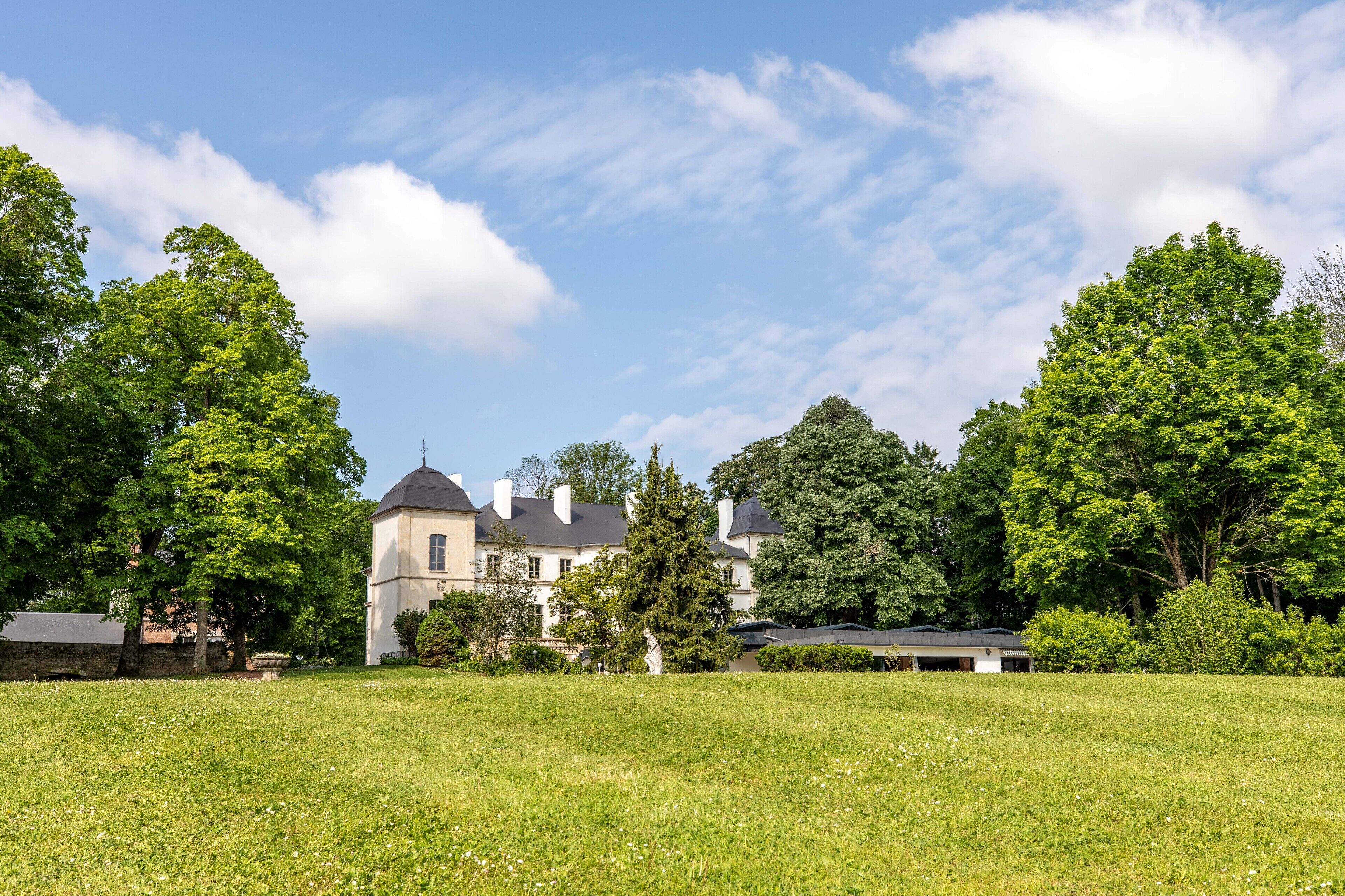 A large, historic building with a symmetrical facade, surrounded by a well-maintained lawn and mature trees.