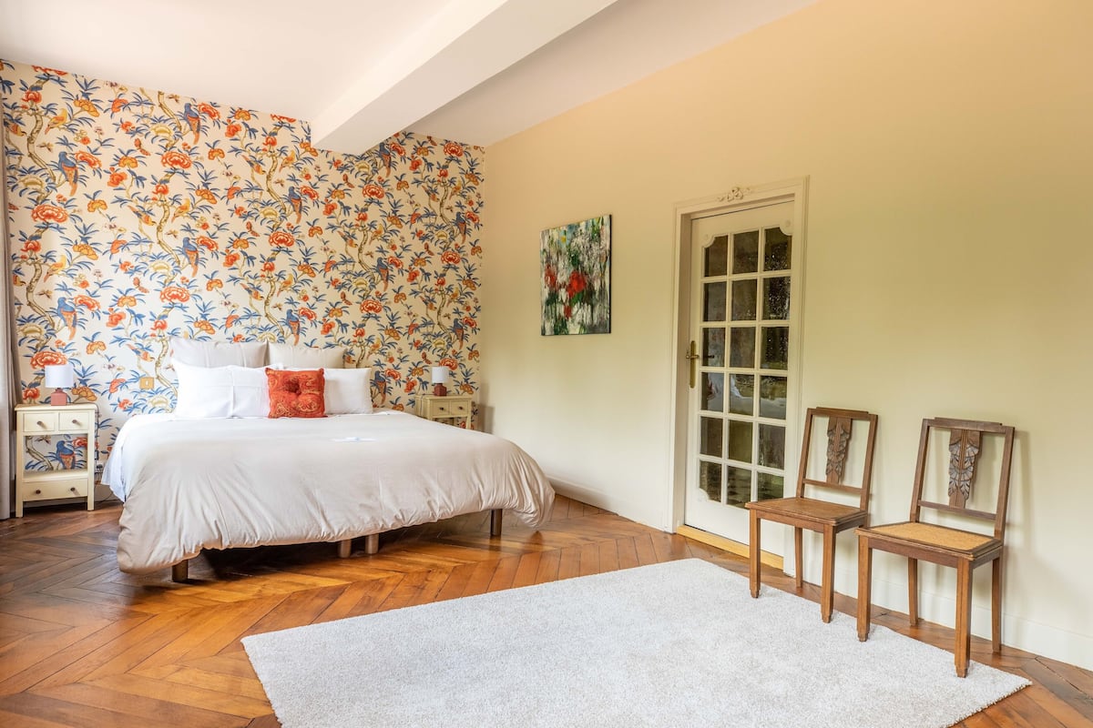Ein Schlafzimmer mit einem Bett, zwei Stühlen, einem Nachttisch und einer Tür.