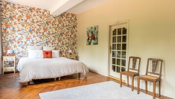 A bedroom with a bed, two chairs, a nightstand, and a door.
