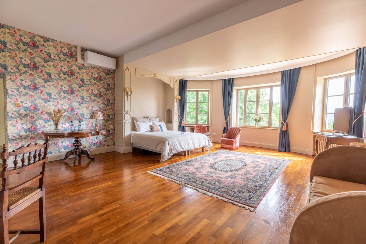 Ein geräumiges Schlafzimmer mit einem großen Bett, einem Holzstuhl, einem kleinen Tisch und einem dekorativen Teppich.