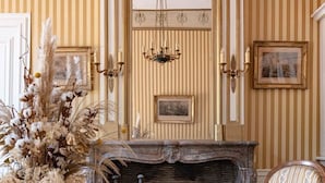 A room with a fireplace, a chair, a glass table, and a vase with dried flowers. - Chambres D'hôtes Vichy : Château de Charmeil (Charmeil)