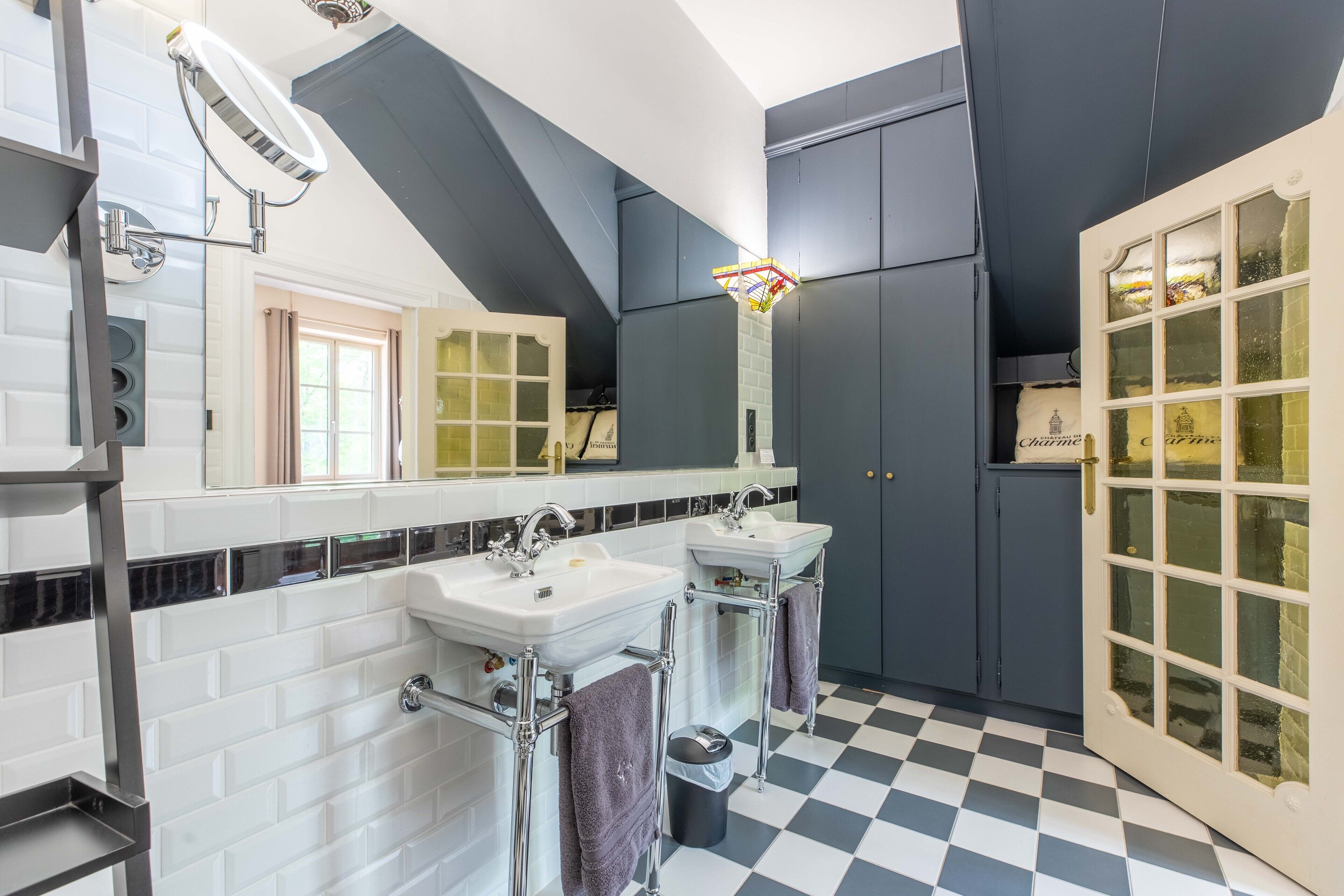Un baño moderno con dos lavamanos, un mueble de tocador, un espejo, una lámpara y un suelo a cuadros.