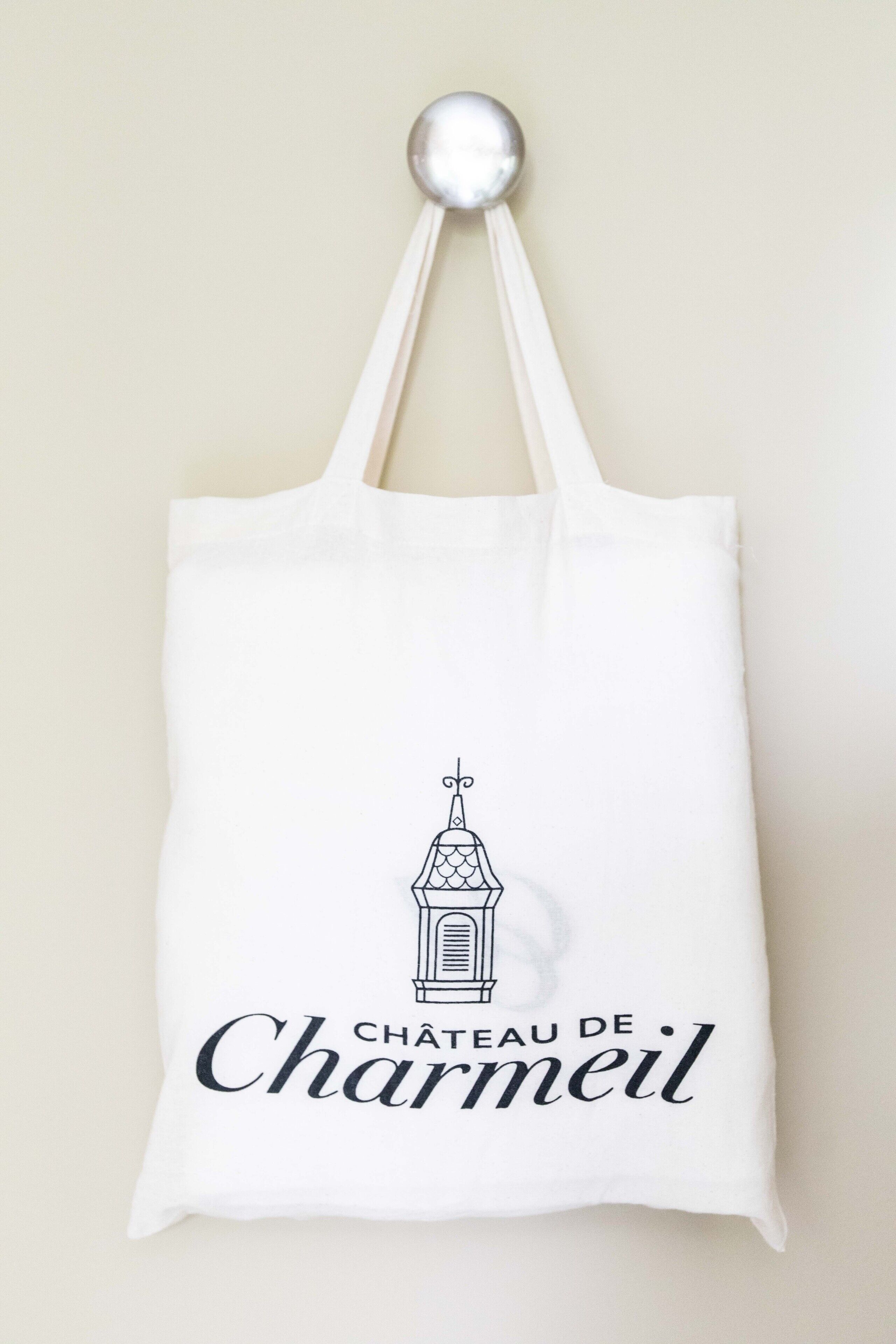 En vit tygkasse med en stiliserad teckning av ett slott och texten ”CHÂTEAU DE Charmeil” tryckt på den.