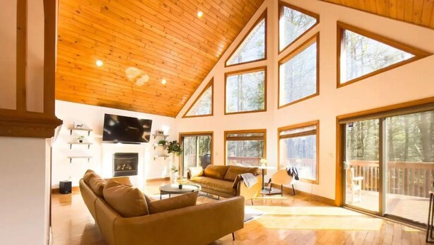 Ein großzügiges Wohnzimmer mit hohen Decken, Holzboden und großen Fenstern mit Blick ins Freie.