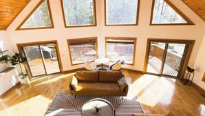 Ein großzügiges Loft mit hohen Decken, großen Fenstern, einer zentralen Sitzecke mit Sofa und Couchtisch sowie Blick auf eine Terrasse und Bäume.