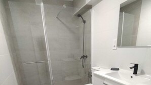 Un baño moderno con cabina de ducha de vidrio, inodoro blanco y tocador blanco con grifo negro.