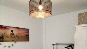 Un dormitorio con cama, lámpara colgante, armario y un cuadro en la pared.