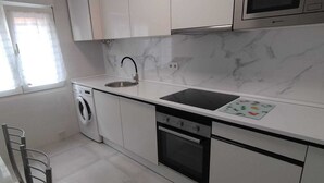 Una cocina moderna con gabinetes blancos, microondas integrado, lavamanos, lavavajillas y lavadora.