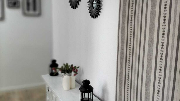 Un pasillo con una consola blanca, espejos decorativos y un panel de tela a rayas.