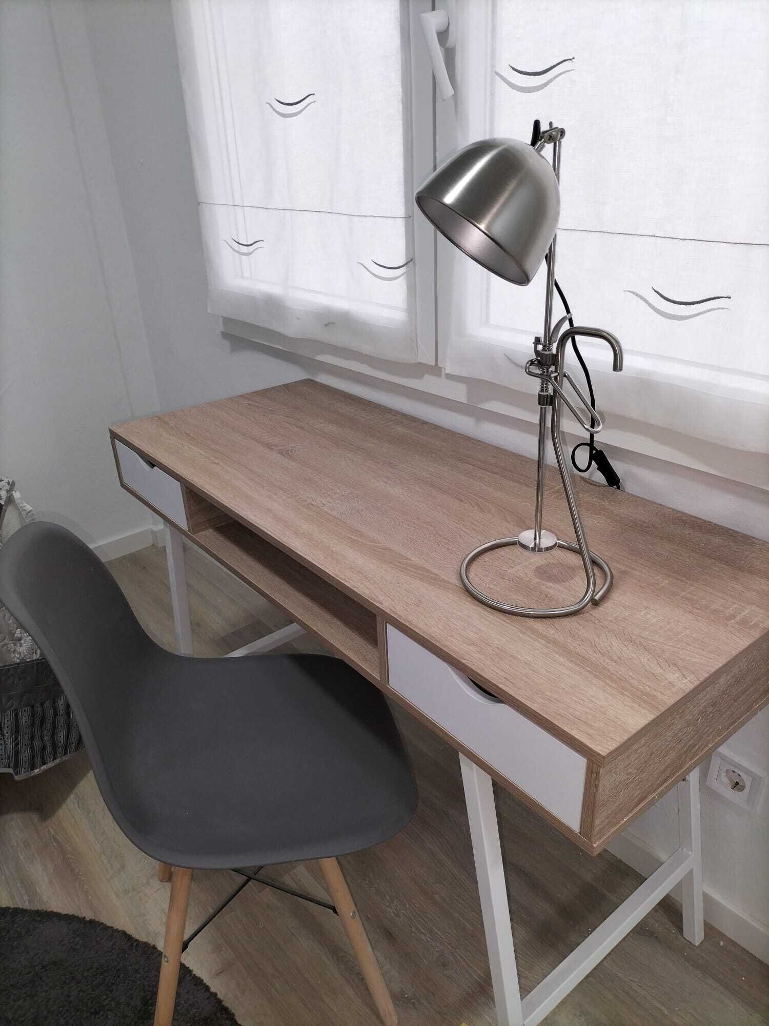 A wooden desk with a chair, a desk lamp, and a window with curtains.