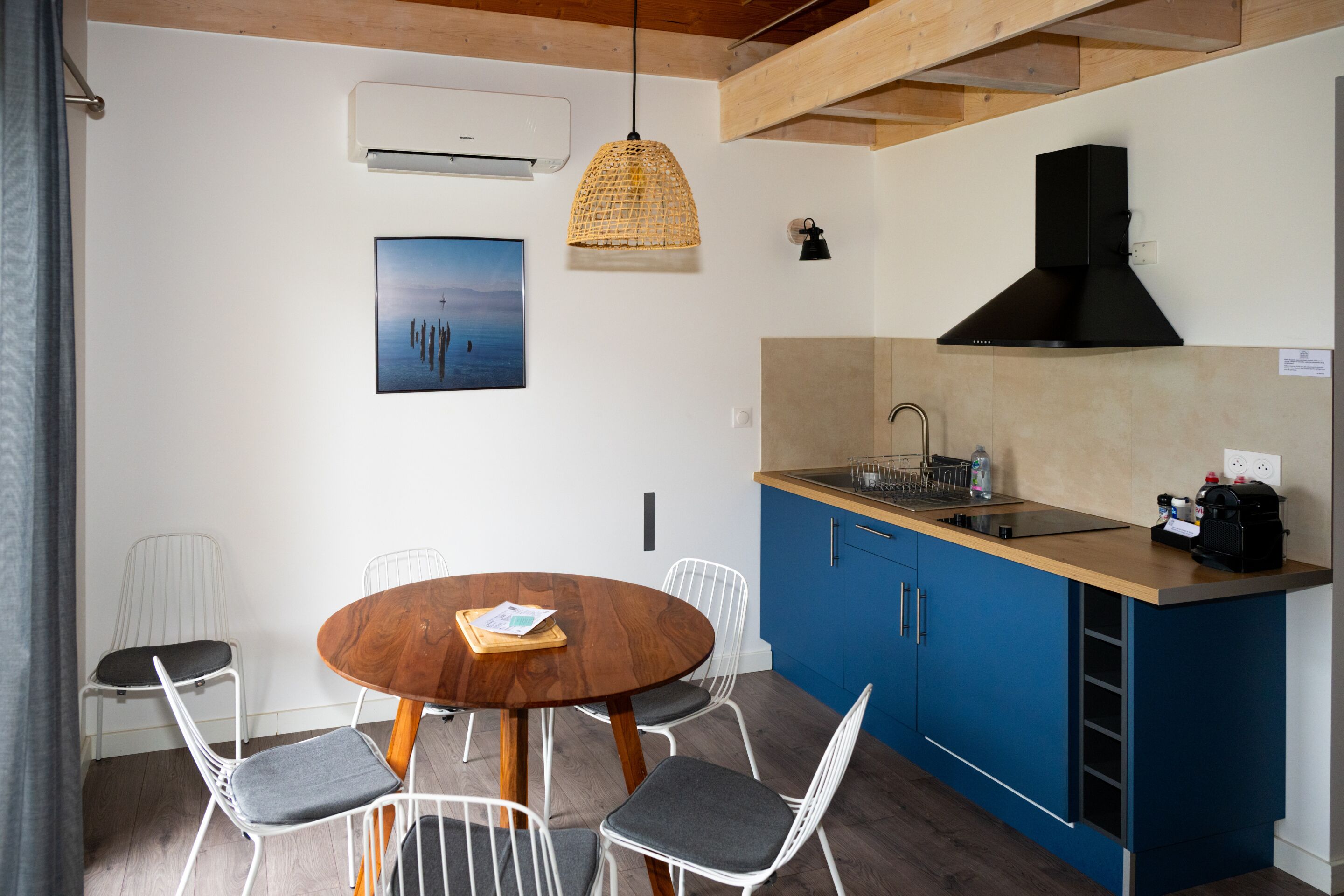 Una cocina compacta con armarios azules, una mesa de comedor de madera y una lámpara colgante.