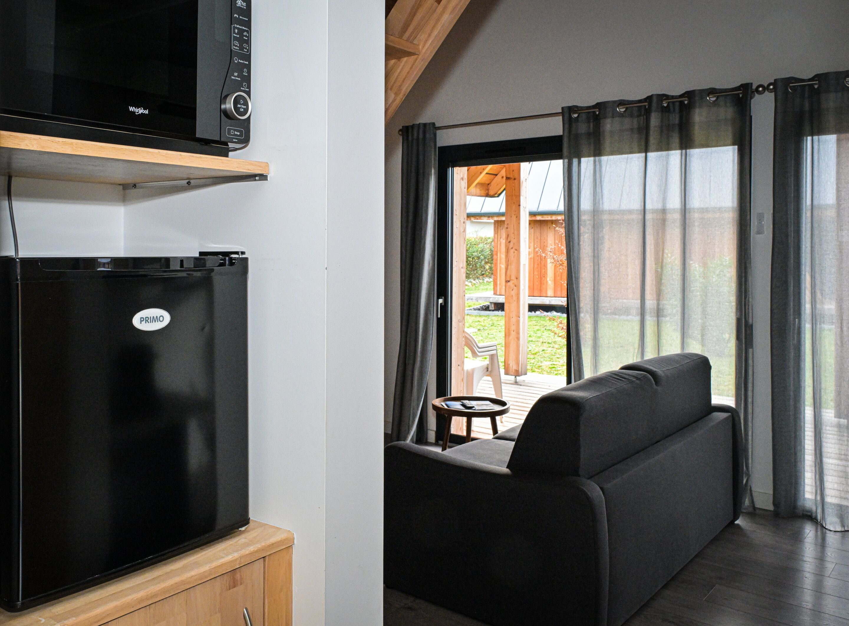 A compact kitchenette with a black refrigerator and microwave, a wooden cabinet below, and a sliding glass door leading to an outdoor patio with a sofa and table.