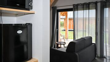 A compact kitchenette with a black refrigerator and microwave, a wooden cabinet below, and a sliding glass door leading to an outdoor patio with a sofa and table.