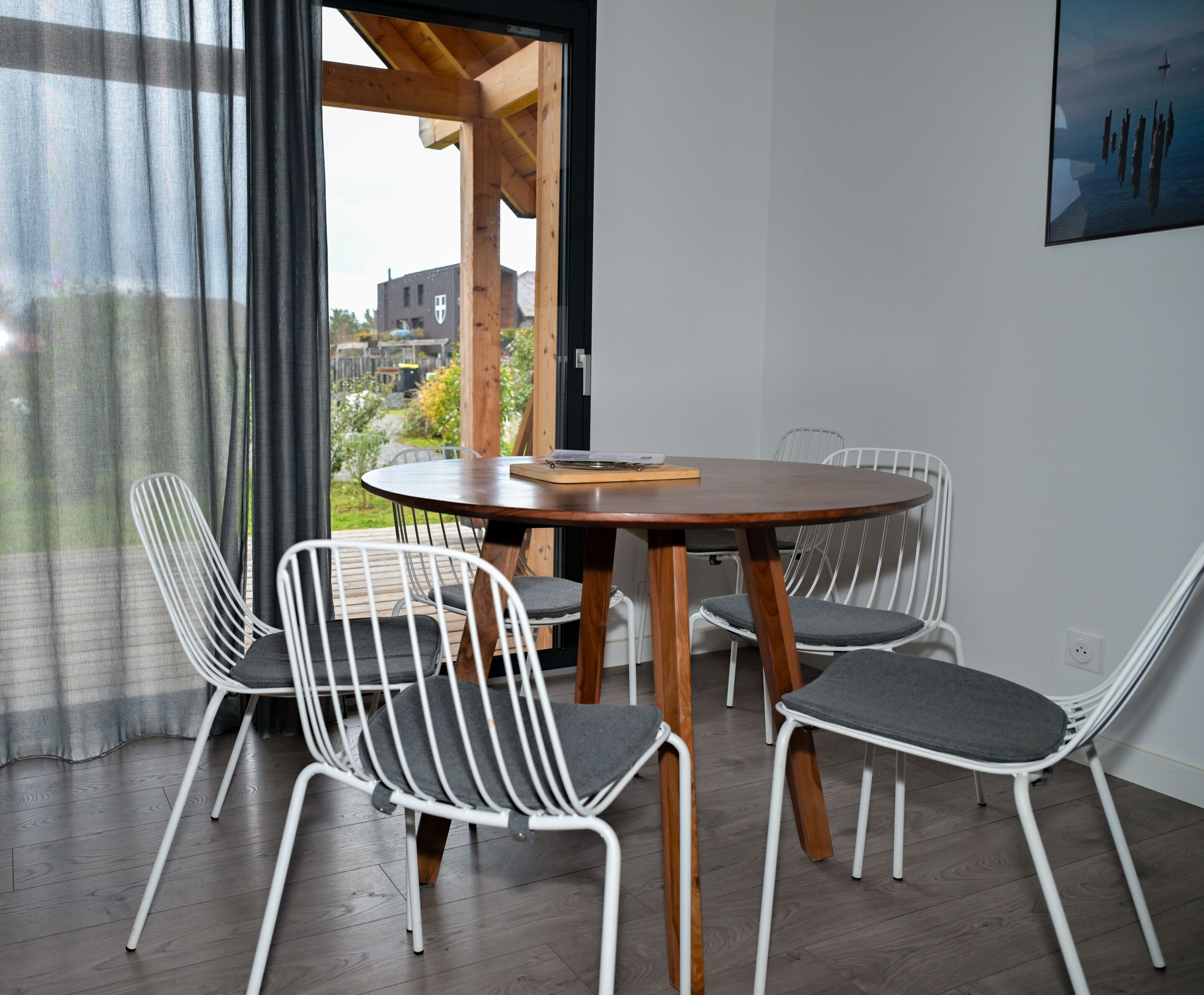 Een moderne eetruimte met een ronde houten tafel en vier witte stoelen met grijze kussens.