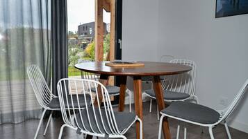 Een moderne eetruimte met een ronde houten tafel en vier witte stoelen met grijze kussens.
