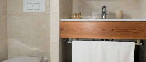 Un baño con inodoro, lavamanos con espejo y un perchero para toallas.