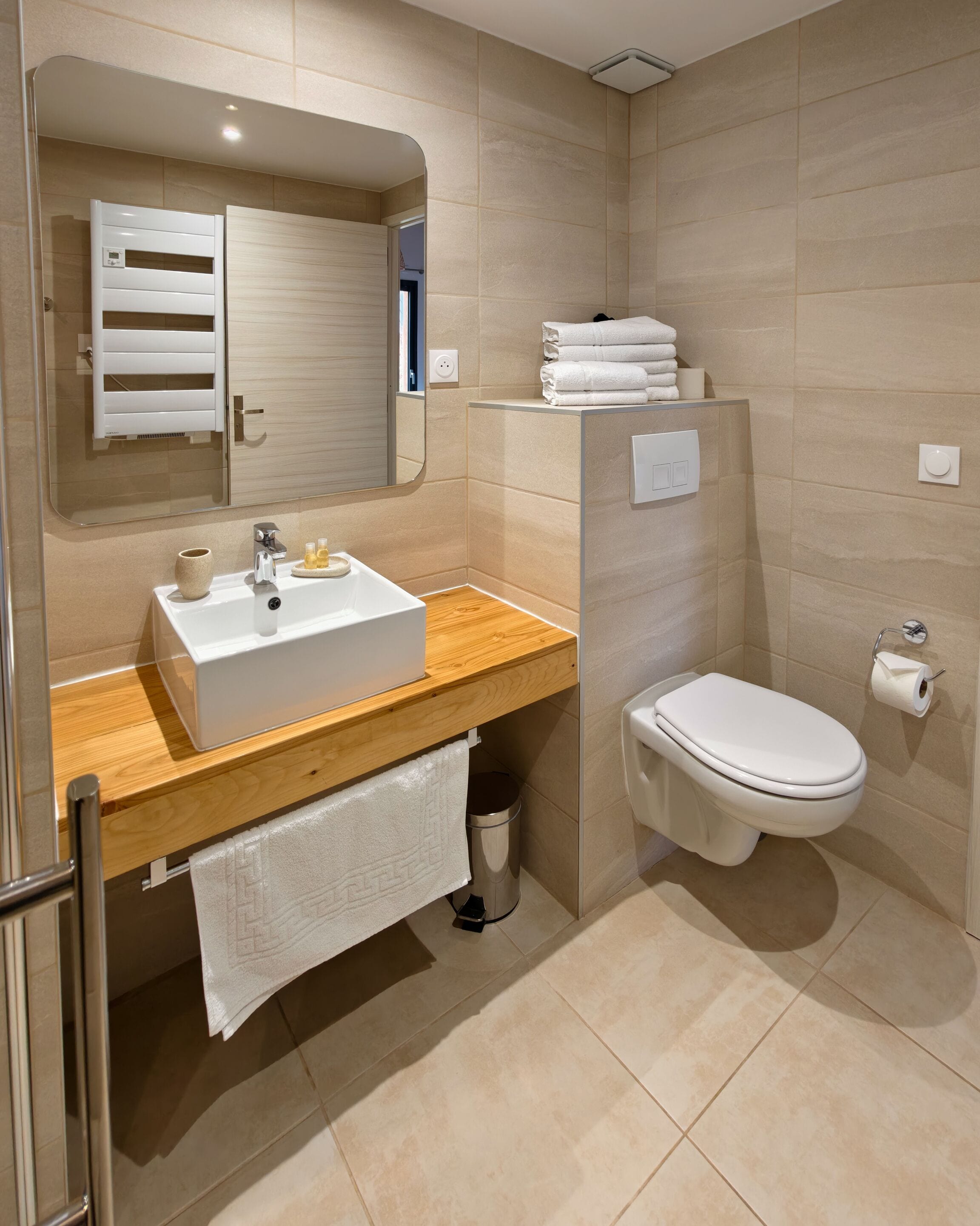 Un baño moderno con tocador de madera, un lavabo blanco, un espejo, inodoro y un perchero para toallas.