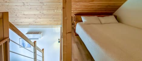 A wooden interior with a bed, a staircase, and a view of a snowy landscape.
