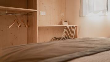 A bedroom with a bed, a wooden wardrobe, a chair, and a desk with a telephone.