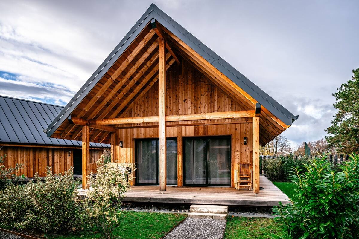 Een modern houten huis met een schuin dak, grote ramen en een houten terras.