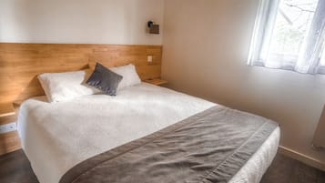 A bedroom with a wooden headboard, a bed with a white and gray blanket, a bedside table, and a window with a curtain.